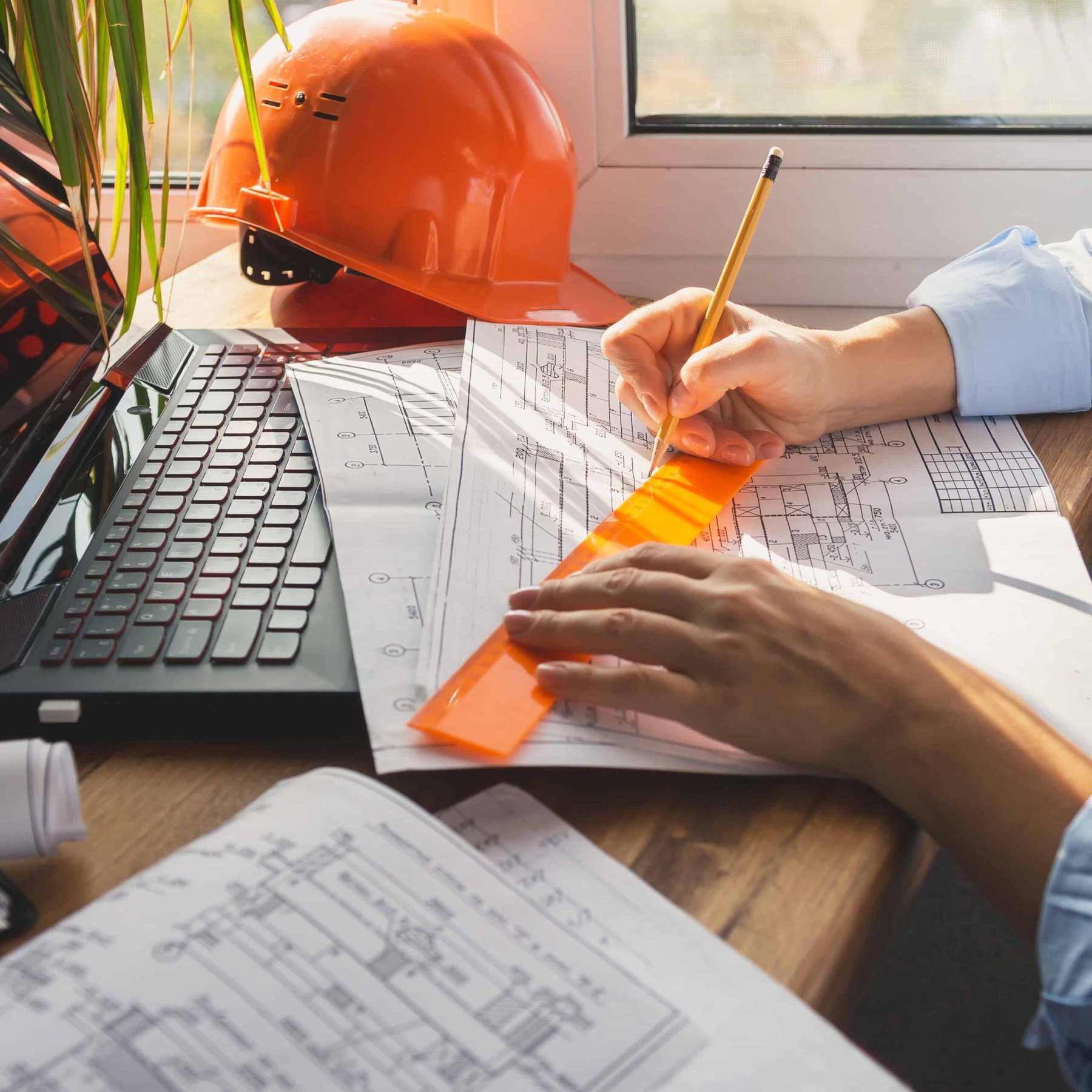 Eine Frau mit Schutzhelm und Laptop arbeitet an Bauplänen für den Kauf oder Verkauf von Immobilien.