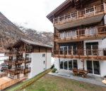 Ein Mehrfamilienhaus in Zermatt mit Balkonen und Blick auf die Berge.