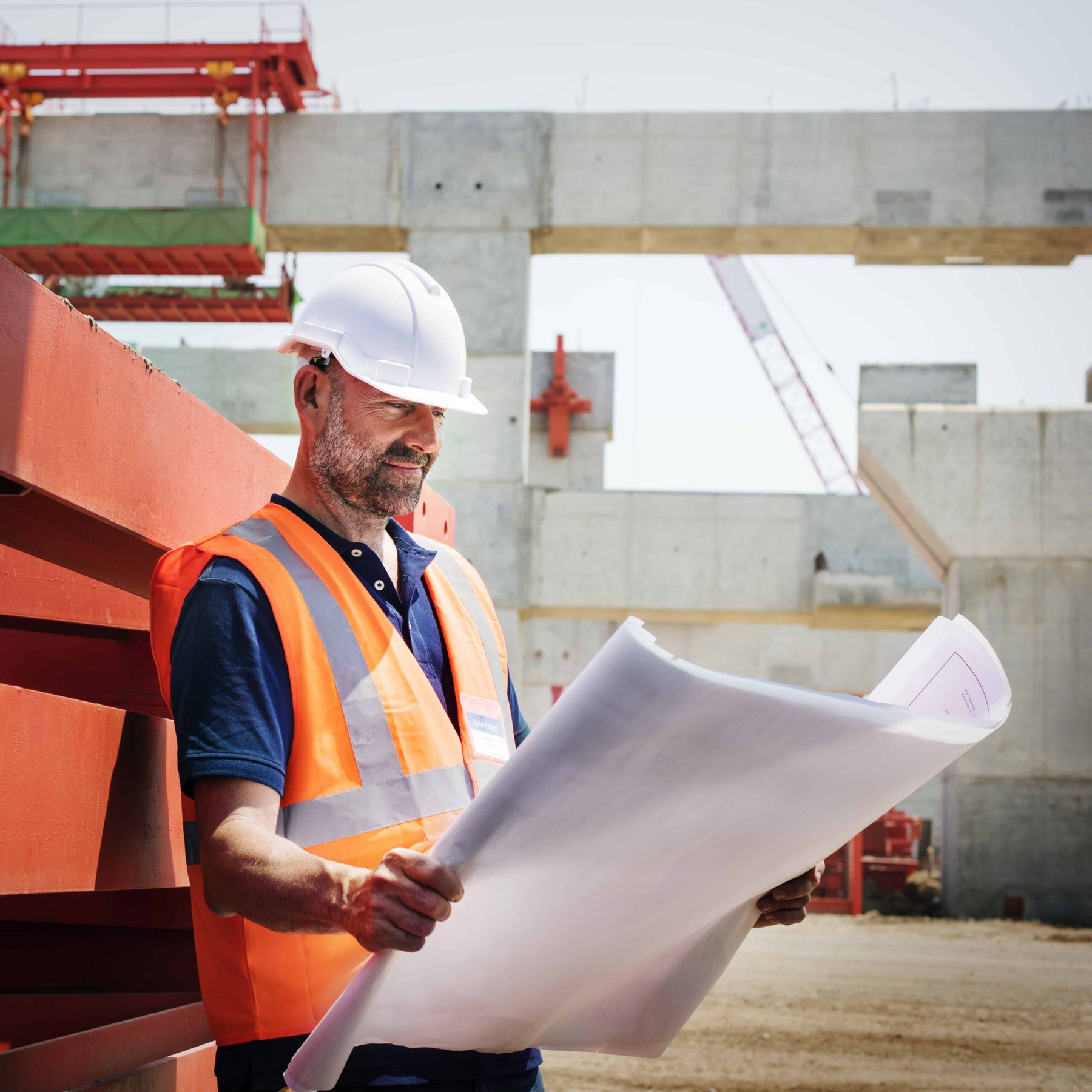 Ein Bauarbeiter hält einen Bauplan vor einer Baustelle in der Hand, während er am Immobilienverkauf arbeitet.